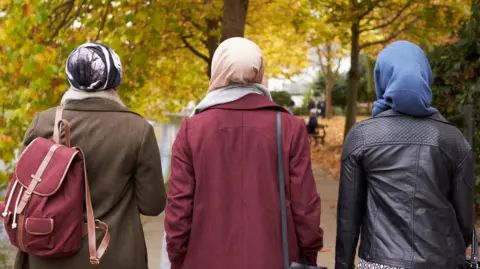 Three Muslim women walking through a park 