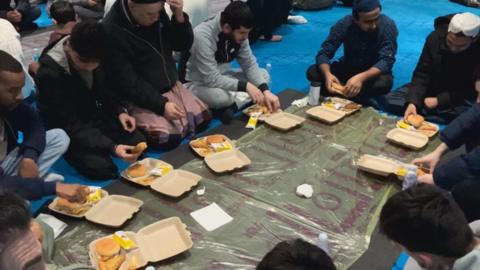Students sitting on the floor eating food from card containers