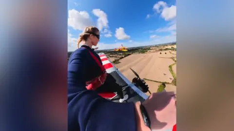 sydney_sweeney/Instagram A blonde woman films herself wing-walking on a bi-plane with fields below.