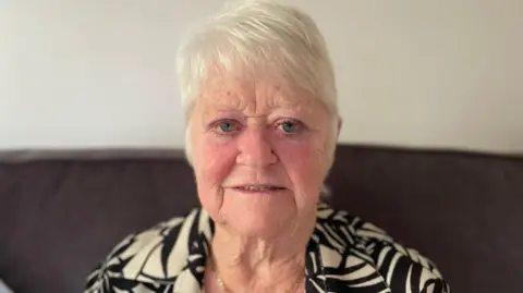 Jean is wearing a black and white top and a necklace