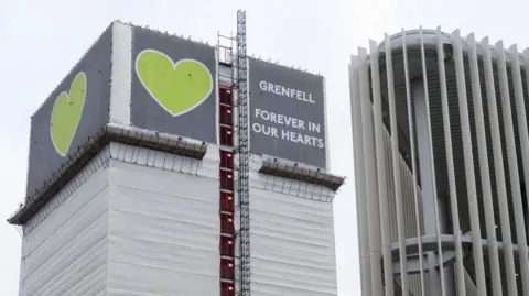 Getty Images The Grenfell Tower with a cover on it. At the top there is a green heart with the wording "Grenfell forever in our hearts"