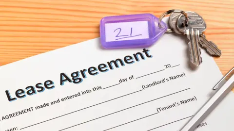 a document that says lease agreement at the top, with a set of keys in the top right hand corner and a silver pen in the bottom left corner. 