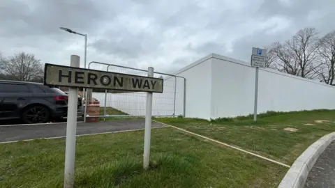 A view of a street sign with white construction fencing in the background.