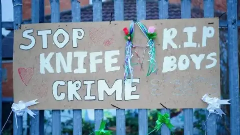 A cardboard sign that says 'stop knife crime' in white letters. it is attached to a metal gate.