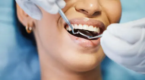 Getty Images Close-up of hands holding dental tools in patient's mouth