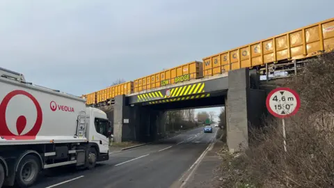 A lorry heads towards a rail bridge as a freight train passes over it.