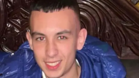 PSNI A young man with short hair smiles, wearing a blue puffer jacket. 