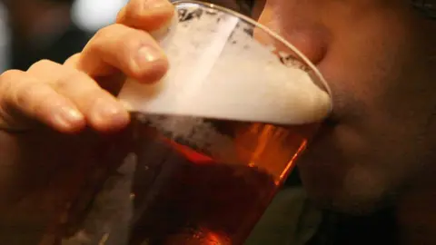 PA Media A man's face pictured close up is drinking a pint of beer
