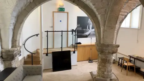 Kit Taylor/BBC Large medieval stone pillars in a soft furnished room.