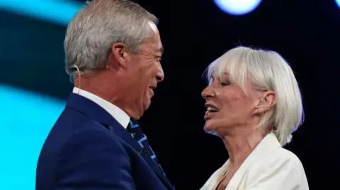 PA Media Reform UK leader Nigel Farage smiles as he greets new recruit and former Conservative MP Nadine Dorries, who defected to Reform, during the party's annual conference at the National Exhibition Centre in Birmingham.