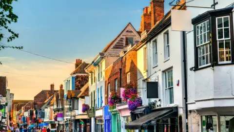 A row of shops in Canterbury City Centre, with the sunlight shining on them.