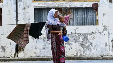 A Rohingya refugee carries her child as she stands at a temporary shelter at a government building in Banda Aceh on December 30, 2023