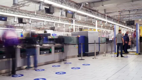 Gatwick Airport A computed tomography (CT) scanner at Gatwick Airport with passengers queueing up to go through security.