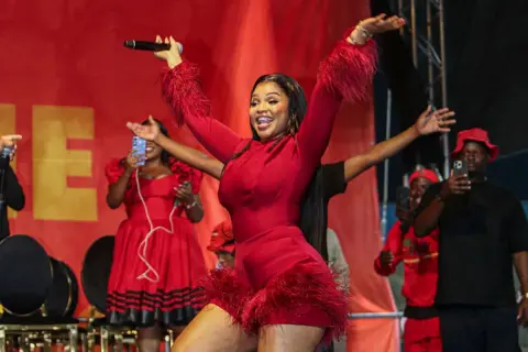 SIYABONGA SOKHELA / GALLO IMAGES / GETTY IMAGES A woman dressed in red stands on stand with her arms in the air.