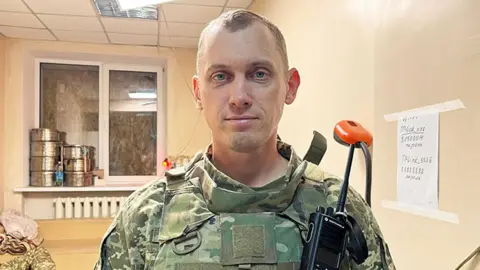 Imogen Anderson/BBC Oleksandr, the head of a medical unit for the Ukrainian army's 25th brigade, photo'd at his place of work, wearing army uniform, and facing the camera in a bare-looking room