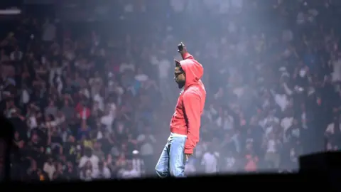 Getty Images Kendrick Lamar performs on stage in jeans and a red hoodie