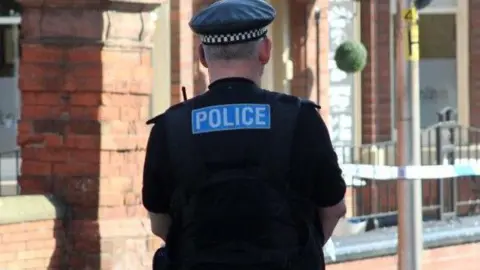 PA Media Police officer dressed in black wearing a peaked cap with black and white checked headband.