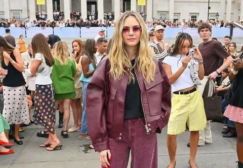 Getty Images for Topshop A model in a velvet pink jacket and black top stands in front of mingled crowds in Trafalgar Square.
