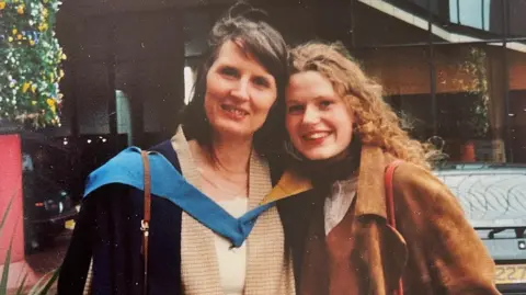 Monica Chatterton Mrs Chatterton and her daughter Josephine are standing with their heads touching as they smile for the camera. The photo was taken after Josephine's graduation ceremony from Huddersfield University. Mrs Chatterton is wearing her daughter's blue academic hood and Josephine is wearing a brown suede jacket.