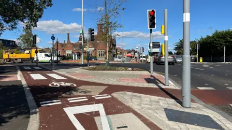 The Cyclops Junction in Cambridge, showing a bike path next to a traffic light, with cars and a pub in the background.