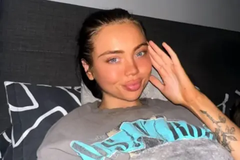 Supplied Image of a woman with dark hair wearing a grey t-shit. She has a tattoo on her left arm. 