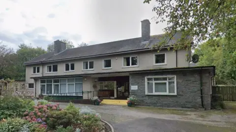 Applethwaite Green Care Home. It is an aging two-storey building. There are flowers in the garden outside the building.