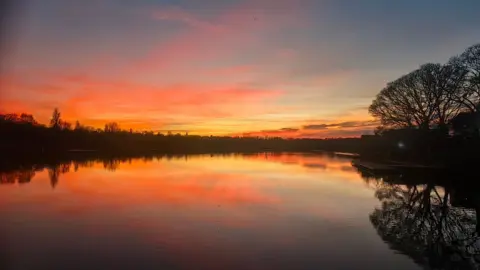 Alison Matthews A sunset reflected on a pool with trees reflected by the water
