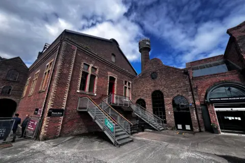 The brick boiler house in front of a large tower against a blue sky.