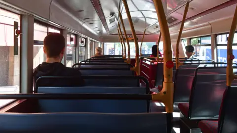 An empty looking bus, with people sat far apart. Taken from the back seat of a bus. 