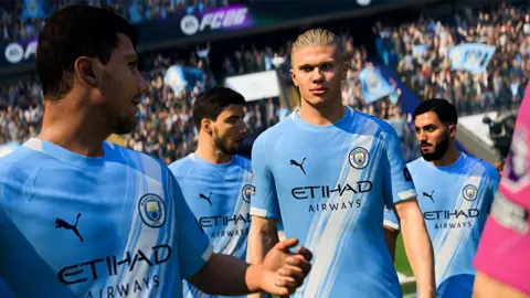 EA Screenshot from EA FC shows a photo-realistic Erling Haaland in his Manchester City home kit walking out on the the pitch alongside his team-mates. In the background a crowd cheers and waves banners.