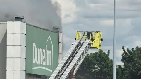 Kirsty Connor Smoke can be seen billowing from a Dunelm store. An extended cherry picker attached to a fire engine is in the shot.