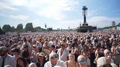 Concert-goers wear bald caps outdoors.