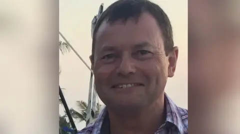 Family handout Simon Healey - a white man who is smiling with a checked shirt and short, dark hair 