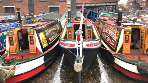 Three colourful narrowboats moored at Ellesemere Port in front of a red brick building.