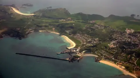 BBC An aerial photograph of Alderney. Green land is visible with a beach and blue water surrounding it.