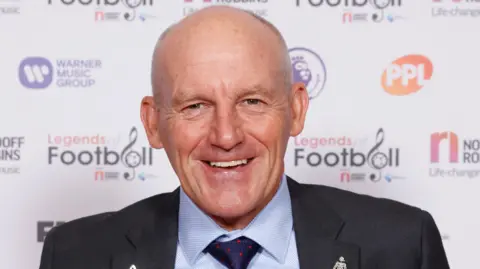 Getty Images Steve Coppell smiling, wearing a dark suit and in front of a white banner which have marks including Legends of Football.