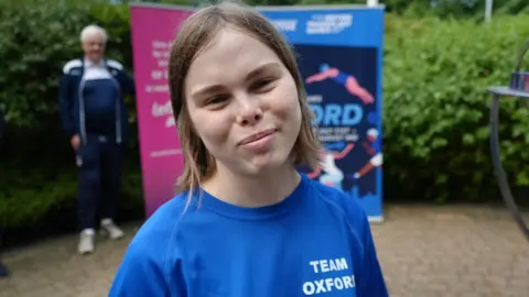 Blossom martin has medium length brown hair and is wearing a blue t-shirt.