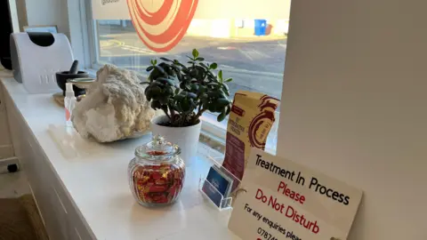 Angelle Joseph/BBC A windowsill inside the clinic which has various items placed upon it including business cards, plants and glass jars.