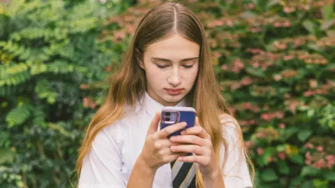 A teenage girl in school uniform stares at a phone