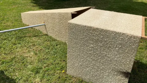 A picture shows the cenotaph toppled over onto the grass, where it has come apart. 