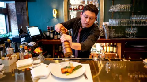 A server grinds pepper over a plate at Le Central restaurant in San Francisco, California, US, on Tuesday, May 7, 2024.