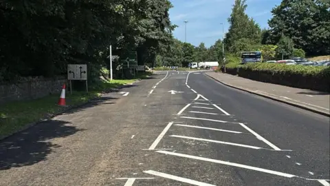 A stretch of freshly surfaced road with trees up either side