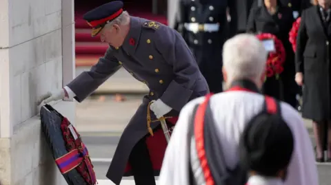 Reuters King Charles, wearing a ceremonial frock coat, places a large poppy wreath which is wrapped in a ribbon on the Cenotaph