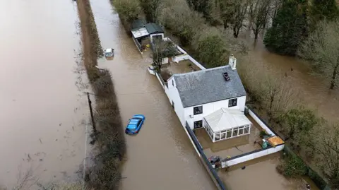 Finnbarr Webster/Getty Images Aerial photo showing a house and car surrounded by heavy flood water