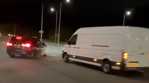 Black BMW drifting close to a white van