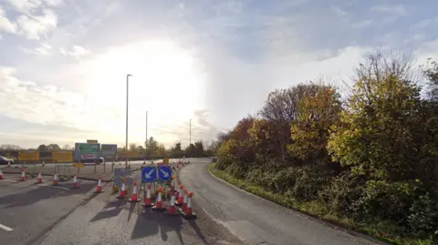 Google A large roundabout with traffic cones and blue road signs across the left hand lane