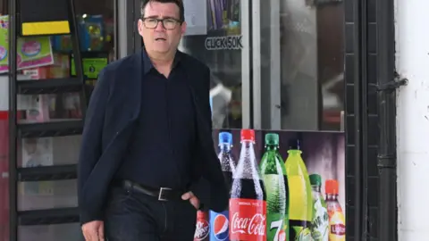 Andy Burnham walking down a street dressed in all black clothes.