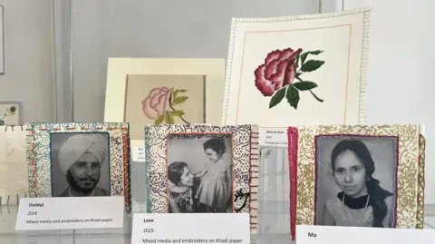 Julita Waleskiewicz A display of mixed-media artworks features black-and-white portraits set in embroidered frames, alongside floral illustrations in the background.