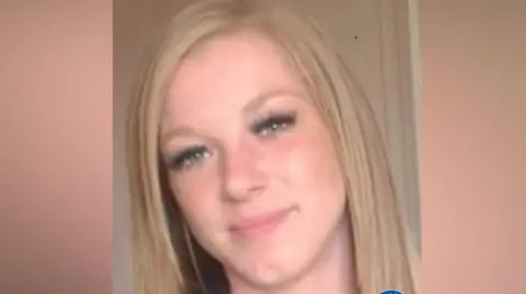 A woman with long blonde hair smiles in a selfie.