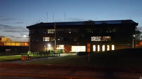 PA Media A dark picture of the outside of HMP Wymott at night. The building is three-storey with lights shining through the windows on the ground foor level
